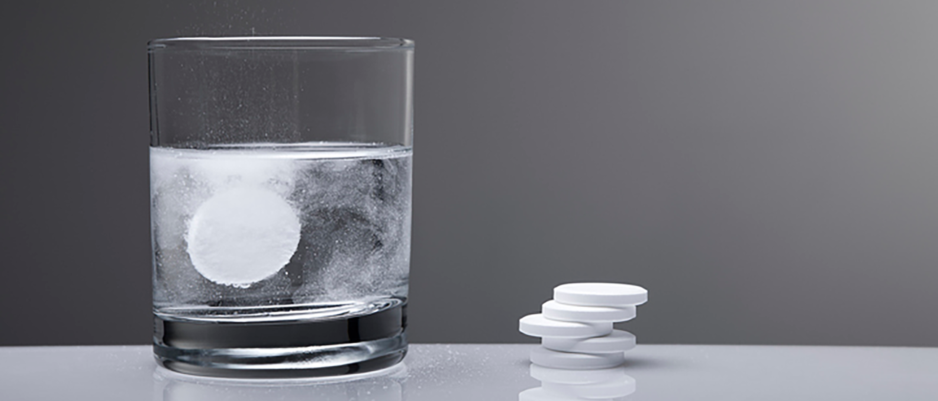 Glas Wasser mit Brausetablette und daneben weiteren Brausetabletten